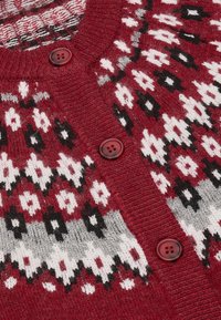 Roter gestrickter Cardigan mit geometrischem Muster in Weiß, Schwarz und Grau; strukturierter Stoff mit vier passenden roten Knöpfen entlang der Vorderseite.