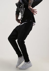 Pantalons de survêtement noirs au design fuselé, avec une texture en panneaux et une taille élastique. Associés à un t-shirt graphique noir et des baskets blanches.