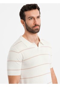 Polo tričko s krátkým rukávem v off-white barvě s světle růžovými horizontálními pruhy. Obsahuje klasický límec a měkkou, texturovanou látku.