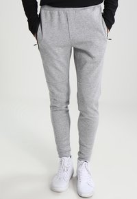 Graue Sweatpants aus weich gewebtem Stoff, mit schmal zulaufendem Schnitt, seitlichen Taschen und elastischem Bund, kombiniert mit weißen Sneakers.