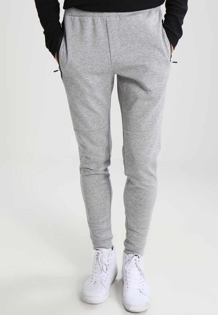 Graue Sweatpants aus weich gewebtem Stoff, mit schmal zulaufendem Schnitt, seitlichen Taschen und elastischem Bund, kombiniert mit weißen Sneakers.