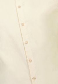 Crème-kleurig button-up overhemd gemaakt van gladde stof, met een rij beige knoopsluitingen aan de voorkant.