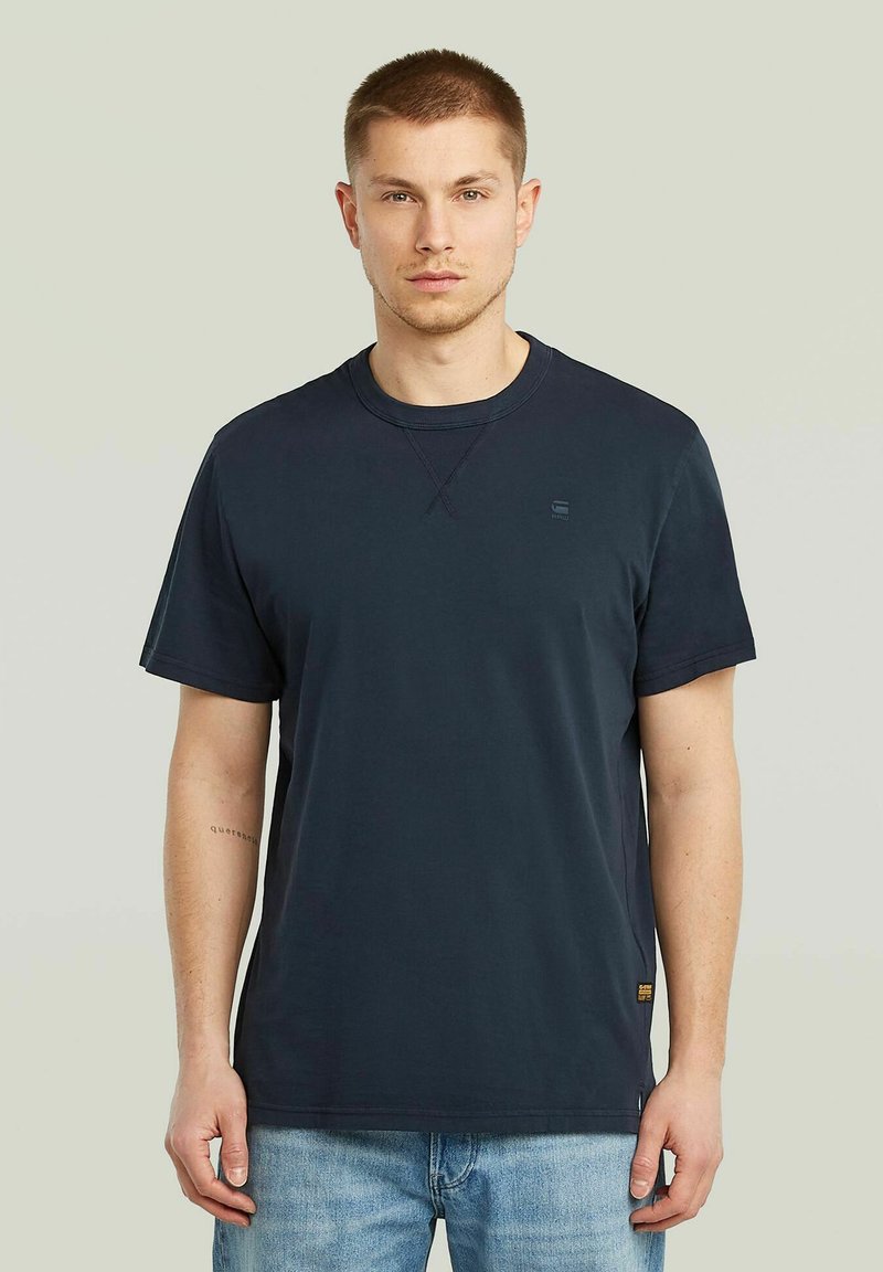 T-shirt in cotone blu navy con maniche corte, collo rotondo e logo piccolo sul petto, caratterizzato da una vestibilità rilassata e dettagli di cuciture visibili.