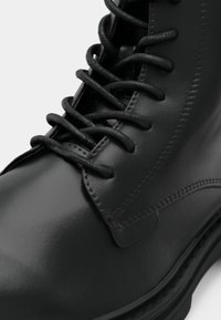 Crna kožna gležnjača sa zaobljenim vrhom, ravnim vezicama i vidljivim šavovima. Glatka tekstura i čvrsti potplat s minimalnim metalnim ukrasima.