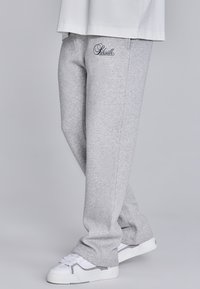 Gaiši pelēki sporta bikses, kas izgatavotas no mīksta auduma, ar pieguļošu dizainu, sānu kabatām un izšuvuma logotipu priekšējā kreisajā pusē.