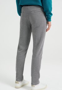 Šedobílé houndstooth kalhoty s úzkým střihem, obsahující dvě zadní kapsy a hladkou texturu látky. Kombinováno s bílými teniskami.