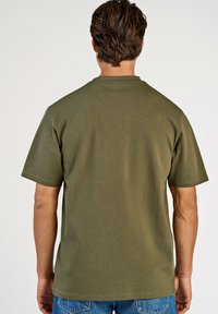 Kortärmad T-shirt i olivgrön bomull, med rund hals och avslappnad passform. Enkelt design utan mönster eller utsmyckningar.