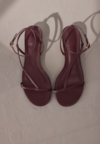 Bordeauxrote flache Sandalen mit schmalen Riemen und einer Knöchelschnalle. Glattes Leder, minimalistisches Design und offene Zehenpartie.