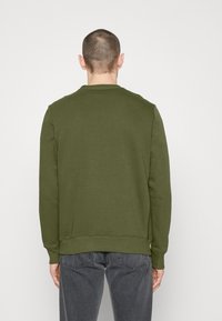 Felpa girocollo verde oliva con maniche lunghe. Texture liscia, polsini e orlo a coste. Indossata con jeans grigio scuro vista posteriore.