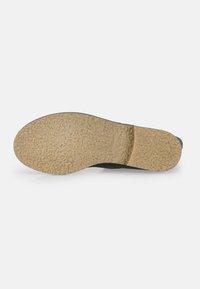 Suela de zapato negra con superficie de goma texturizada, tacón afilado y una suela exterior de color marrón claro con un ligero brillo y detalle de marca.