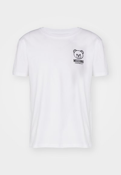 Baltas kokvilnas T-krekls ar īsām piedurknēm, apaļu kakla izgriezumu un melna lāča grafiku ar tekstu "Moschino Underbear" uz krūšu daļas.
