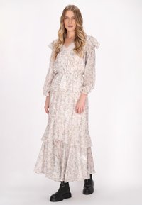 Lungo vestito fluente in tessuto leggero e trasparente con un motivo floreale. Presenta maniche arricciate, una vita elastica e un orlo a strati. Stivali neri.