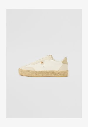 Sneaker beige in tela con suola in juta intrecciata e texture, dotato di un design liscio con lacci e un piccolo logo di accento sul lato.