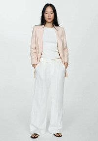 Light pink blazer over a white top, paired with loose white trousers and black sandals. Smooth fabric with classic collar and wide-leg design.