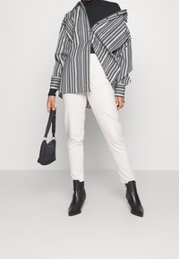 Camisa de rayas en blanco y negro de corte oversized, combinada con pantalones ajustados blancos. Botines negros y un pequeño bolso negro completan el look.