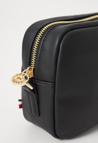 Trousse de maquillage en cuir noir avec fermeture éclair dorée et breloque en forme de clé décorative. Présente une texture lisse et un design compact et rectangulaire.