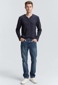 Camiseta henley de manga larga azul marino con tejido texturizado, con tapeta de dos botones; se lleva con vaqueros azules y zapatillas blancas.