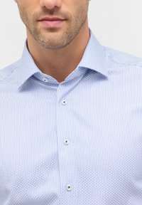 Lichtblauw shirt met een verfijnend geometrisch patroon, voorzien van een spread collar en knoopsluiting. Gladde stof met een subtiele glans.