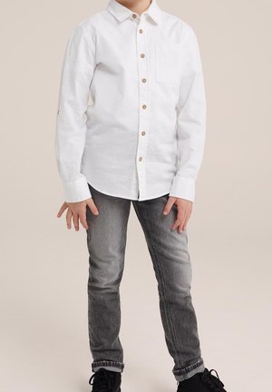 White long-sleeve button-up shirt with wooden buttons, featuring a chest pocket. Paired with gray jeans and black sneakers.