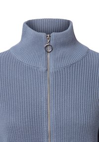 Sweter z dzianiny zapinany na zamek w jasnoniebieskim kolorze, z wysokim żebrowanym kołnierzem. Posiada srebrny zamek błyskawiczny oraz teksturowany materiał o jednolitym wzorze.