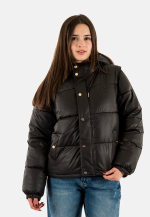 Schwarze Pufferjacke mit Kapuze, goldenen Knöpfen, Seitentaschen und gestepptem Struktur. Trägt man über hellblauen Jeans.