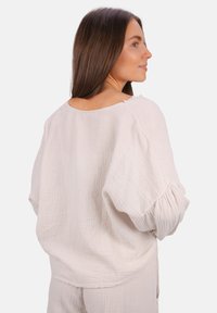 Hellbeige Langarmshirt aus strukturiertem Stoff, mit einem lockeren Schnitt, weiten Ärmeln und einem Rundhalsausschnitt mit dekorativen Nähten auf der Rückseite.