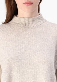 Beige Strickpullover mit hohem, geripptem Kragen. Die weiche Textur und subtile Sprenkel verbessern das Gesamtbild. Kurze Ärmel sind kaum sichtbar.