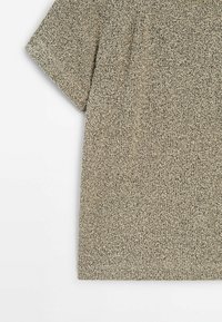 Chemise en tissu beige chiné à manches courtes tricotée, posée à plat avec détails visibles aux épaules et aux manches.