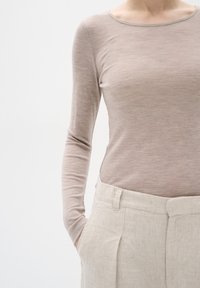 Maglietta a maniche lunghe di un leggero beige con scollatura a barca, abbinata a pantaloni larghi in lino chiaro caratterizzati da un tessuto testurizzato e tasche laterali.