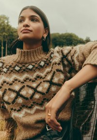 Megztinis su aukštu apykakliu, šiltais rudos spalvos atspalviais ir geometriniais raštais kremine bei tamsiai ruda spalvomis. Lygus paviršius, laisvas siluetas.