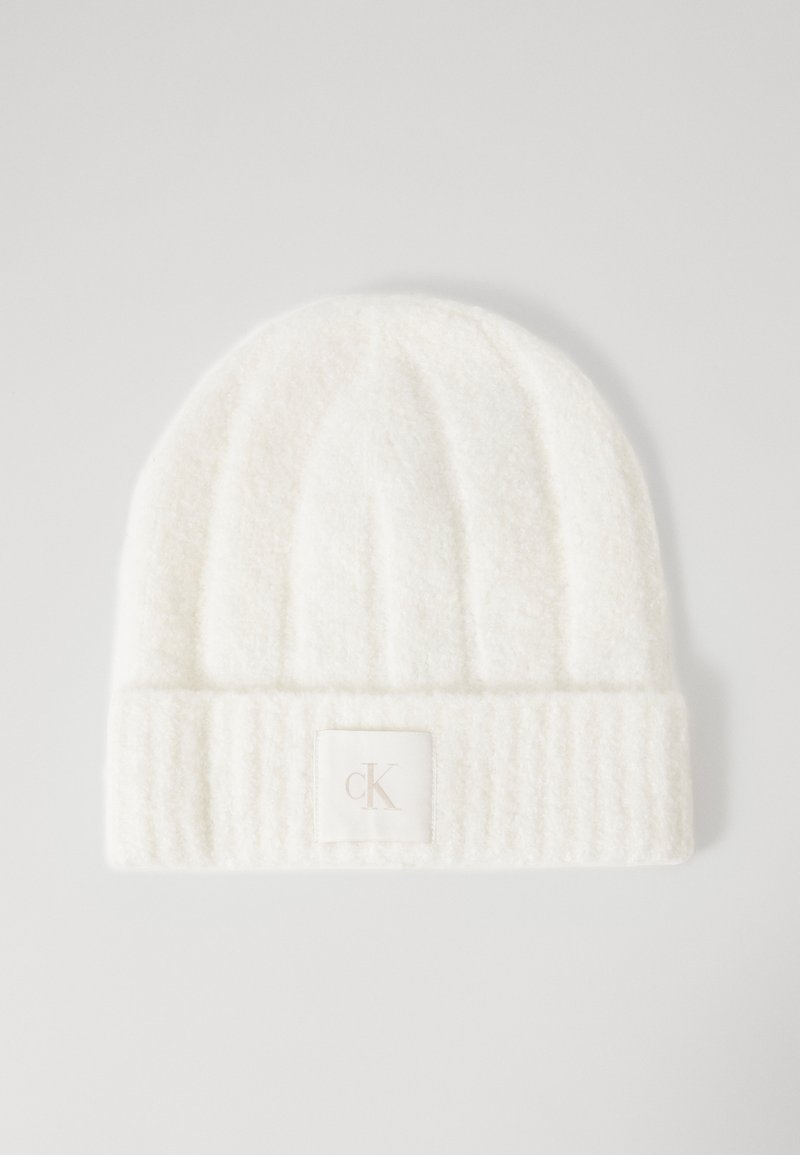 Bonnet en tricot blanc avec un motif en relief, texture douce et un patch logo carré présentant "CK" en couleur claire sur le revers.