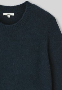 Pull en maille bleu marine avec un col rond et des bords côtelés, dotés d'une texture douce et d'un léger effet duveteux.