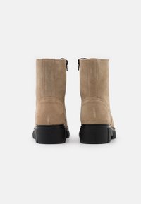 Botines cortos de ante beis con una textura suave, suela de goma negra y cremalleras traseras. Diseño simple y redondeado sin cordones visibles.