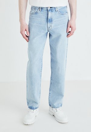 Light blue denim jeans with a relaxed fit, five-pocket design, and visible stitching. Worn with white, chunky-soled sneakers.