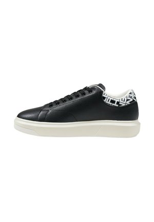 Baskets en cuir noir avec une semelle en caoutchouc blanc, présentant une finition texturée, un design à lacets et des accents motifs au niveau du talon.