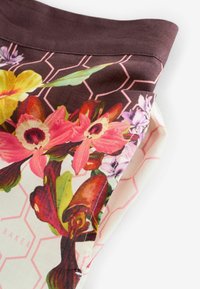 Tuvplāns brūnas un krēmkrāsas audumam ar rozā ģeometrisku rakstu un krāsainu ziedu apdruku uz salocītas apģērba malas.