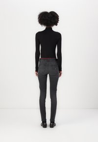 Suéter negro de cuello alto acanalado con mangas largas, combinado con jeans ajustados de color gris oscuro. Detalles notables incluyen una cinturilla roja y zapatos negros.