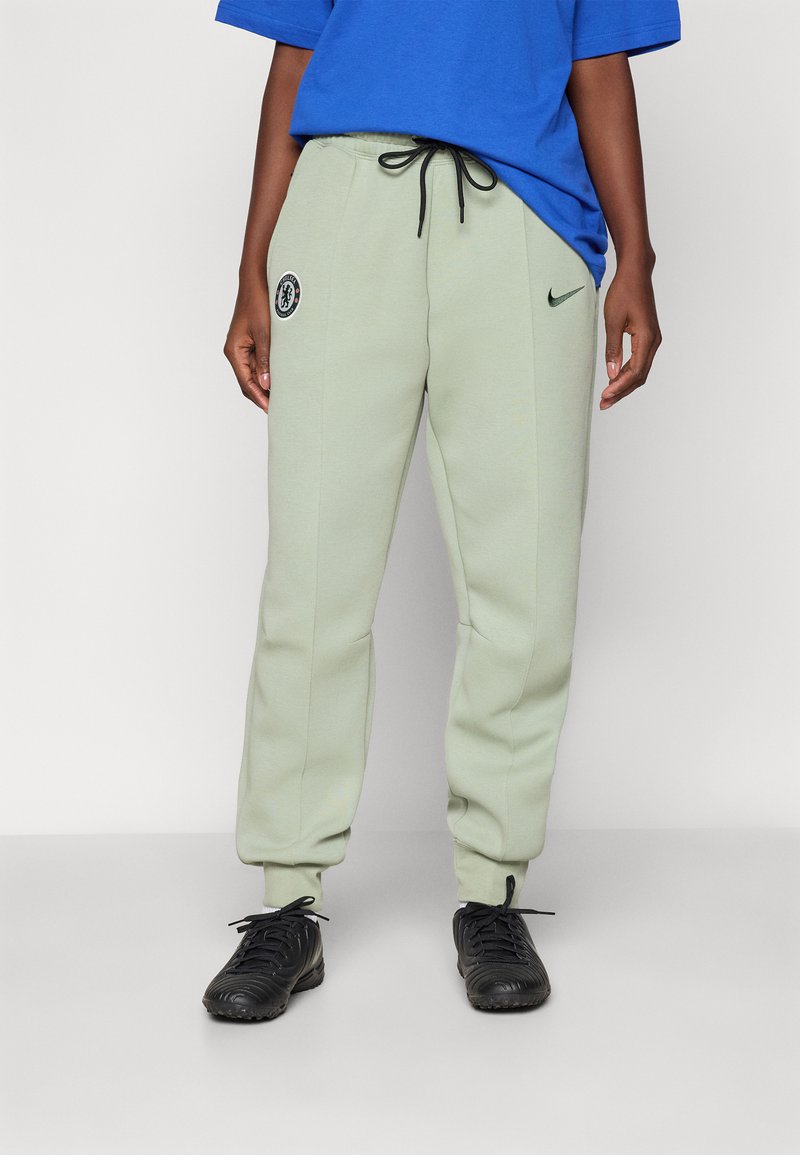 Lysegrønne Nike joggebukser med snøring i livet, sidelommer, Chelsea FC-logo og avsmalnende anklene. Kombinert med sorte treningssko.