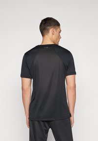 Sort T-shirt med kortærmer til sport, lavet af et glat materiale, med rund halsudskæring og raglanærmer. Logo på den øverste del af ryggen.