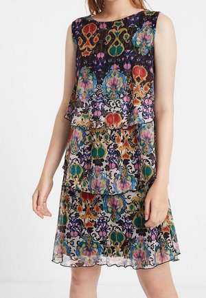 Ærmeløs lagdelt kjole med farverige blomster- og abstrakte mønstre i nuancer af blå, rød, grøn og lilla på sort og hvid baggrund.