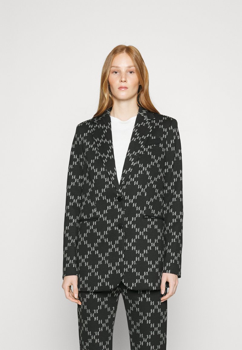 Blazer nero con un motivo geometrico bianco, design strutturato, due tasche frontali, chiusura con un solo bottone, pantaloni abbinati con lo stesso motivo.