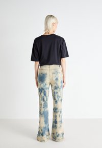 Camiseta negra de manga corta combinada con jeans acampanados de tie-dye en beige y azul, con un patrón en los jeans y un corte relajado.