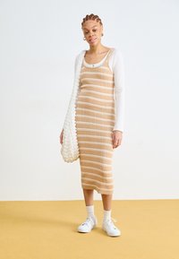 Strikket midikjole i beige med hvite striper, kombinert med en hvit langermet topp og en teksturert kremfarget skulderveske. Hvite sneakers og sokker.