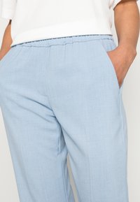 Pantalon bleu clair, ample, avec une texture douce et une taille élastique ; doté de poches latérales et d'une finition en tissu lisse et subtile.