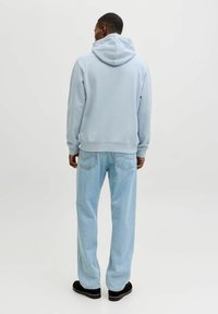 Vaaleansininen huppari, jossa rento istuvuus ja pehmeä pinta. Yhdistetty vaaleansinisiin leveälahkeisiin farkkuihin ja mustiin jalkineisiin.