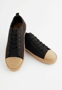Mustad mustad tennisjalatsid, millel on jute aktsendid varvastel ja kummist talla, ümar varvas, paelad ja tõmbeaas kandadel.
