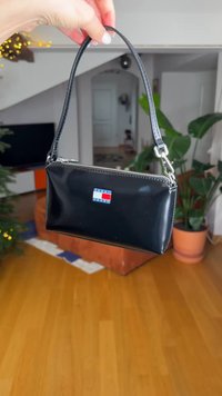 Sac à main en cuir verni noir avec fermeture éclair, garnitures argentées et un logo "Tommy Jeans" bleu et rouge bien visible sur le devant.