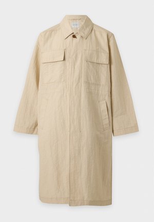 Long manteau beige à col pointu, fermeture boutonnée, manches longues et quatre poches sur le devant, présenté sur un fond uni.