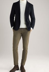 Laivastonsininen bleiseri, jossa on viiltoherneet, tekstuuritettu kangas, paritettu valkoisen neulekauluksen ja khakin slim-fit-housujen kanssa. Ruskeat suedesandaalit.