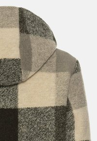 Karierter Kapuzenmantel mit großen Quadraten in den Farbnuancen Creme, Grau und Schwarz. Weiche Textur mit glatter Oberfläche und sichtbaren Nähten.